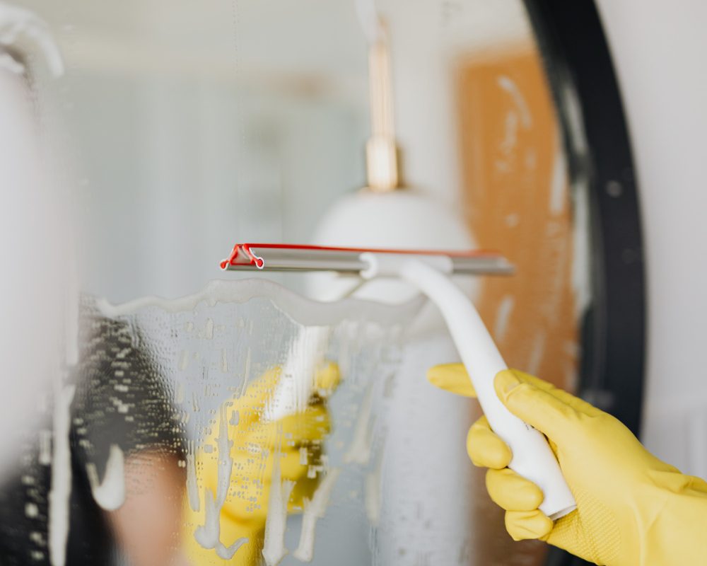 A person in yellow gloves cleaning a mirror.